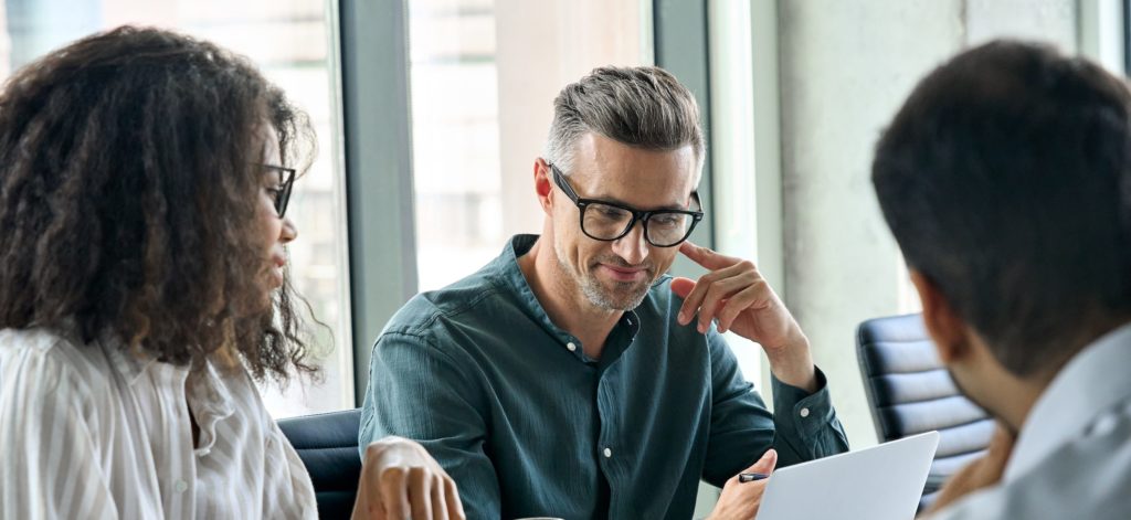 a man and woman at a conference table look at a laptop screen