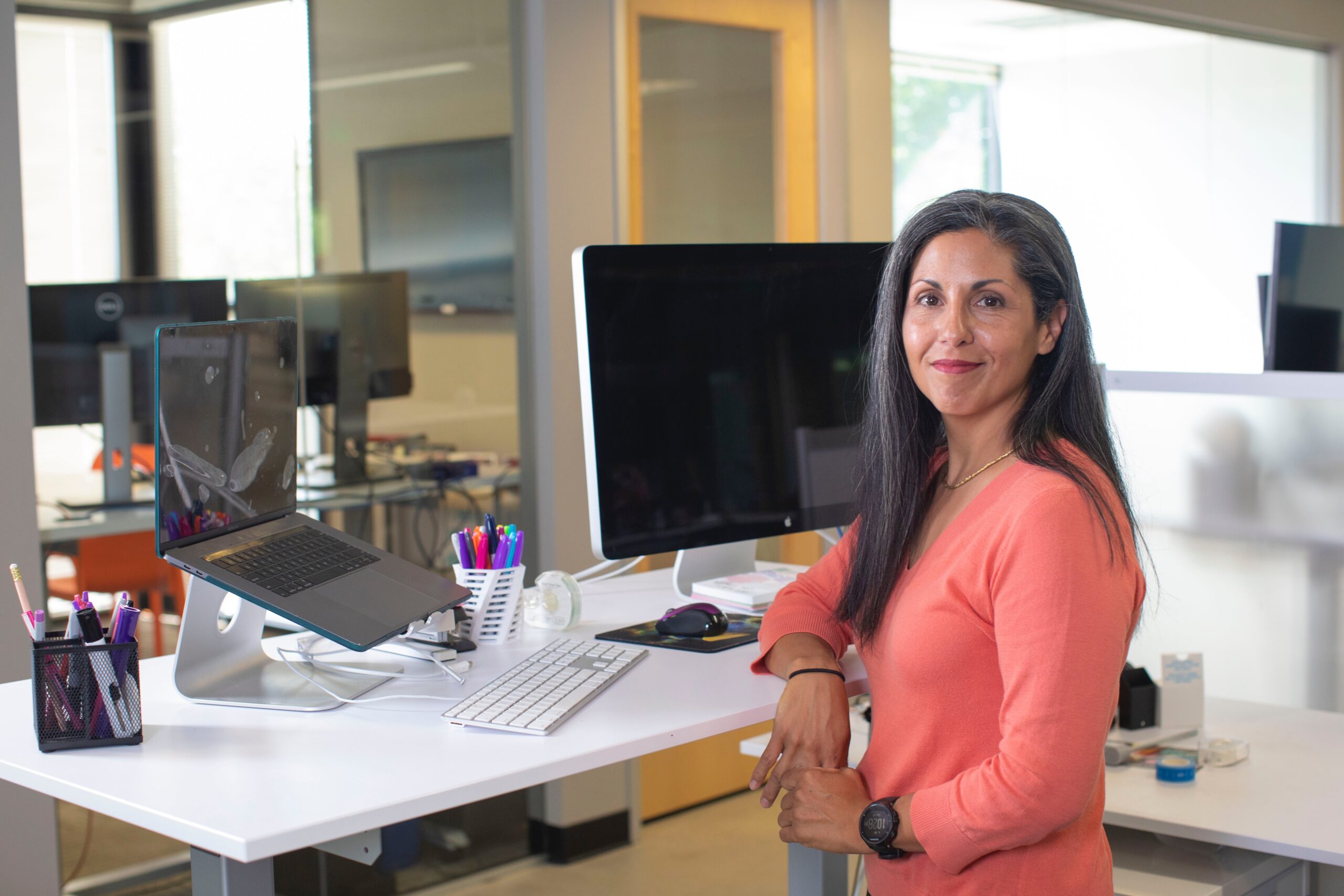 a woman at a standing desk looks at the camera confidently