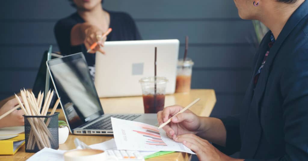 closeup of a busy conference table with one colleague pointing at a datasheet to illustrate the idea of sales enablement best practices