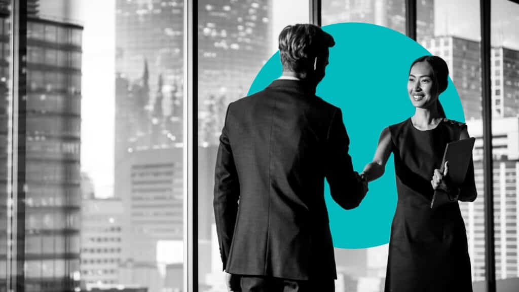 An asian woman and man in business attire shake hands in an urban setting, illustrating how to align sales and marketing.