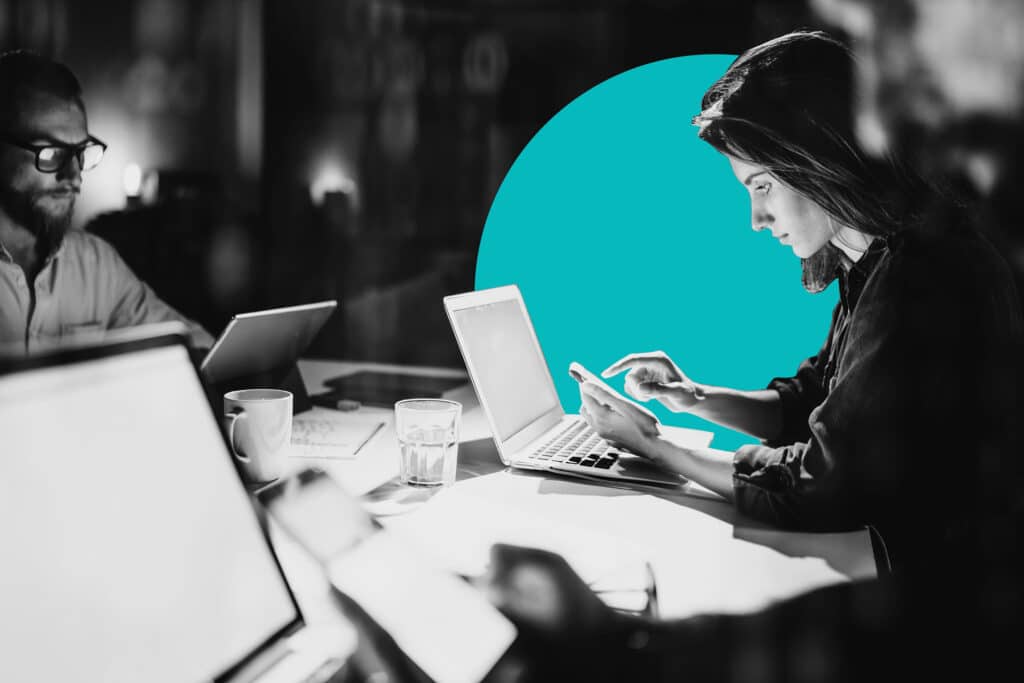 In a dark office, coworkers collaborate on sales and marketing software at a cluttered conference table.